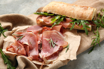 Sliced prosciutto with tasty sandwich and herbs on napkin