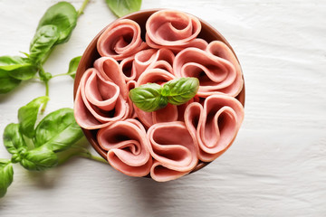 Bowl with delicious sliced and rolled ham on wooden table, top view