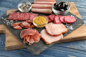 Slate plate with variety of delicious deli meats with spices on wooden board