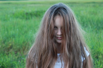 Naklejka premium Girl with long disheveled hair on the background of green grass in nature