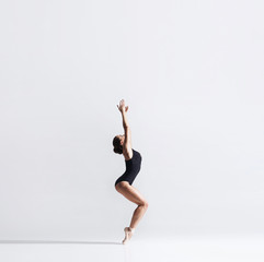 Ballerina in point shoes and bodysuit is dancing in studio. Young and graceful ballet dancer.