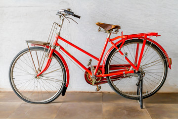 Old red bicycle stand on near wal.