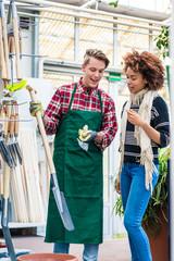 Handsome and cheerful worker wearing a green apron while helping a customer with choosing a...