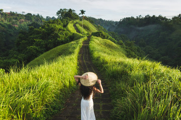 Naklejka premium Młoda piękna kobieta chodzenie po drodze Campuhan Ridge artystów, na Bali, Ubud. Piękny spokojny słoneczny poranek