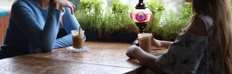 girlfriends enjoying in cafe together. Young women meeting in a cafe. meeting two women in a cafe for coffee. blue dress, dress in a flower, on a carved table is a cups of coffee and a lamp.