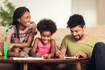 Mom and dad drawing with their daughter. African american family spending time together at home.