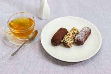 Three chocolate pastries with different sprinklings and cup of tea