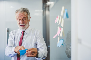 Old senior business man happy working in office, reading sticky note post it in room