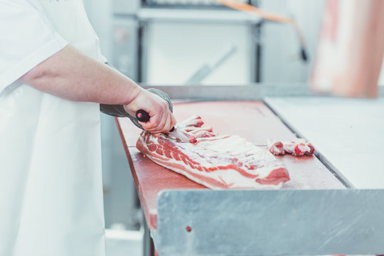 Butcher cutting meat for further processing with knife in butchery