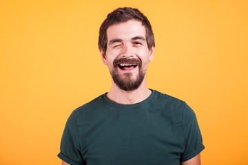 Happy positive man looking at the camera and winking isolated on yellow background