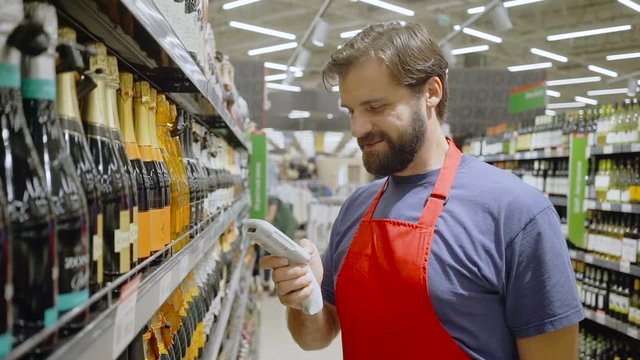 supermarket employee in red aport scanning barcode at wine section in supermarket