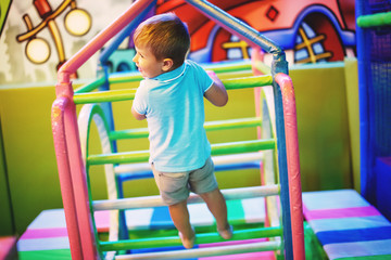 Fototapeta premium Cute little boy in a blue T-shirt is playing on a children's playground indoors.