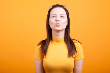 Pretty girl making kiss to the camera on yellow background