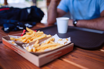 Selective focus paper tray with fried potatoes on a wooden desk in a restaurant with blurred man in the background