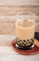 A glass of sweet milk bubble tea with tapioca pearls, and straw on wooden background. Copy space