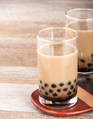 A glass of sweet milk bubble tea with tapioca pearls, and straw on wooden background. Copy space