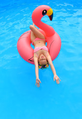 A young woman spends leisure time in a pool on  an inflatable sun bed . She wears a red polka dot bikini and has sunglasses on. 