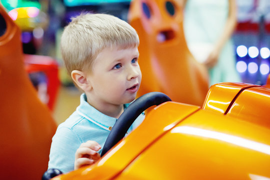 Cute Blond Little Boy Driving Car Arcade In Game Machine At An Amusement Park.