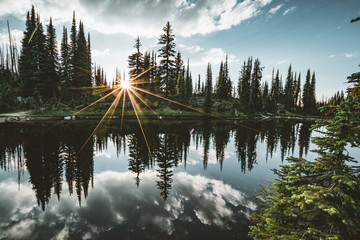 Lake on the summit of Mount Revelstoke sunset reflection sunstar across forest with blue sky and...