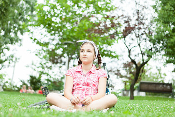 Happy teenager girl sitting on the grass in the park next to her bicycle