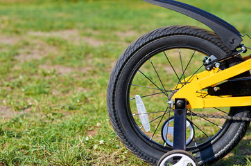 Fototapeta na wymiar Kids yellow bicycle in park, close up parts, rear tire with brakes and additional wheels