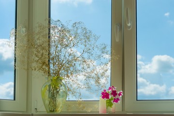 Window in apartment, house, view of blue sky with clouds. On the windowsill vase of flowers, home real life.