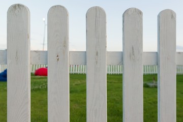 Decorative wooden fence painted white. A green lawn behind fence.