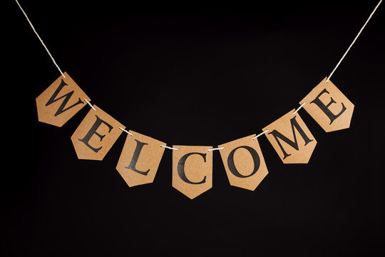 Welcome Home Banner. Greeting With The Word Welcome Written In Letters Hanging On A Bunting String. Isolated Against Black Background.