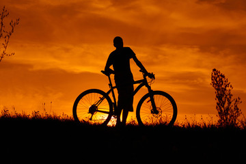 Silhouette of a young man with a bicycle at sunset.