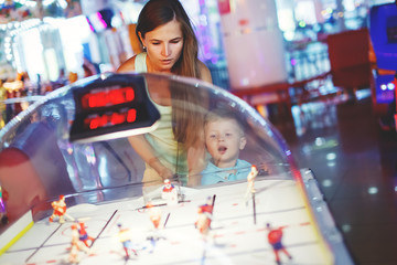 Family mother and little boy playing table hockey arcade in game machine at an amusement park.