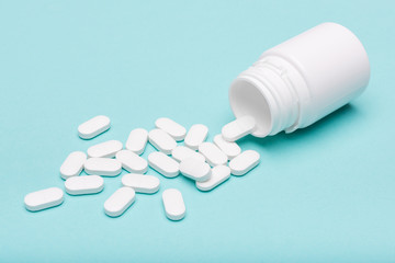 Medication bottle and white pills spilled over blue pastel colored background. Medication and prescription pills background. Pharmaceutical drugs.