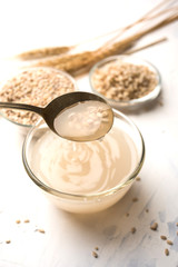 Barley water in glass bowl with spoon and raw and cooked pearl barley wheat/seeds. selective focus