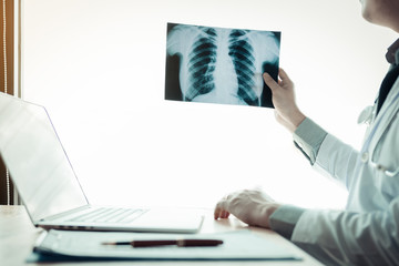 Doctor holding x-ray film at lap in hospital office.