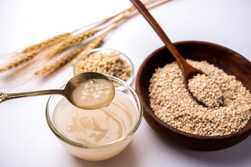 Barley water in glass bowl with spoon and raw and cooked pearl barley wheat/seeds. selective focus