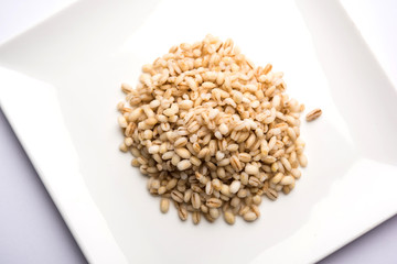 Raw and cooked Barley pearl seeds in a bowl or over white plate. selective focus