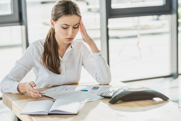 overworked young businesswoman with headache doing paperwork at office