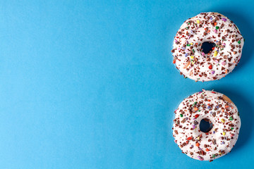 Two white donuts with colorful sprinkles on a blue background