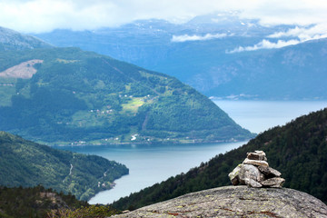 Stone cairn in Husedalen valley with cascade of four waterfalls, Kinsarvik, Norway