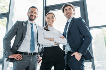 Fototapeta premium bottom view of group of smiling young business people standing at modern office and looking at camera