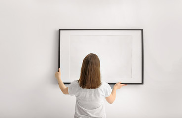 Woman hanging blank photo frame on white wall