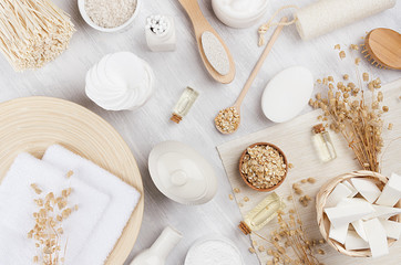 Fototapeta na wymiar Handicraft natural cosmetics - white cream, oil, towel and bath accessories on soft light white wood table, flat lay.