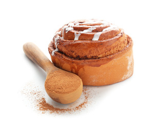 Tasty sweet bun and spoon with cinnamon powder on white background