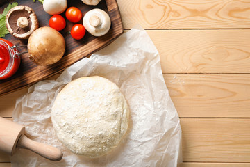 Composition with raw dough and ingredients for pizza on wooden background