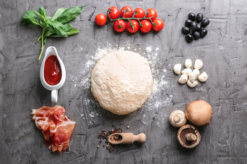 Composition with raw dough and ingredients for pizza on grey textured background
