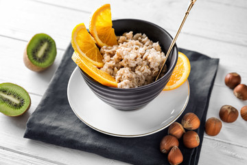 Bowl with tasty oatmeal on white wooden background