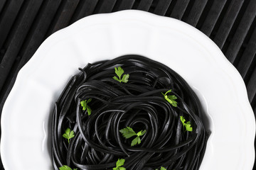 Pasta with wheat germ and black squid ink. Black pasta and parsley on a white plate. Macro. Top view.