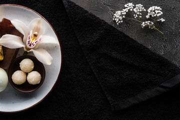 top view of beautiful white flowers, homemade scrub and black towel, spa treatment concept
