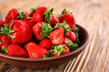 Plate with ripe red strawberries on wooden table, closeup