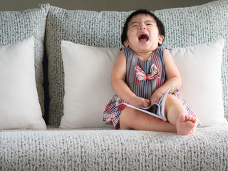 Happy little cute girl is reading the book on the white sofa. Education, Children, Family Concept.