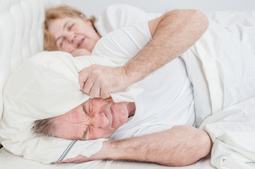 Fototapeta na wymiar The elderly man covered his ears with a pillow so as not to hear the snoring of his wife